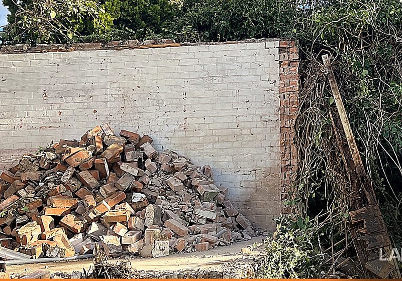Failed brick boundary wall with a collapsed section and a pile of rubble at its base