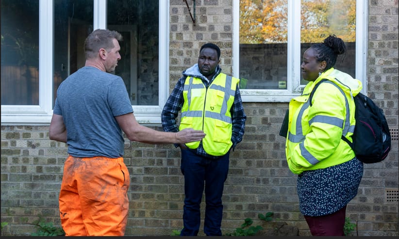 Two Ora Labora structural engineers in hi-vis jackets discussing a residential property survey with a builder outside a brick house